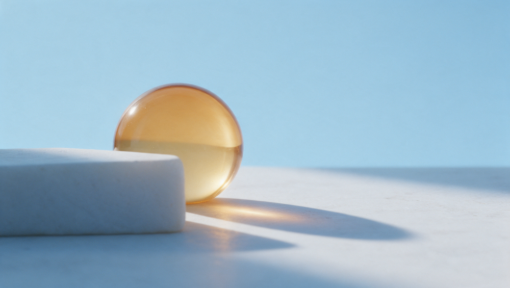 Sphère de verre ambré à demi cachée derrière un bloc de pierre claire, comme un soleil bas d'hiver, sur fond bleu ciel
